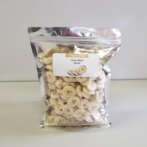 May include: A silver resealable bag filled with freeze-dried banana slices. The bag has a white label that reads "Freeze Dried Coco-Nana Slices".