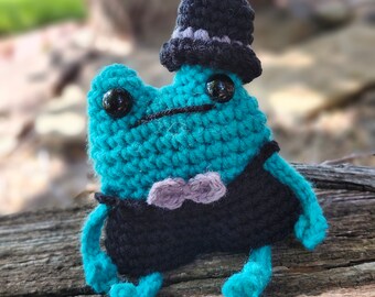 Handgemaakte gehaakte kikkerknuffel: amigurumi met lange benen en hoge hoed