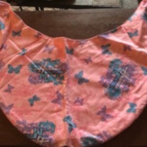 May include: Pink fabric tote bag with a butterfly and floral print. The bag has a large opening and a single handle.