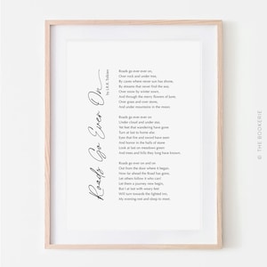 May include: A framed print featuring the poem "Roads Go Ever On" by J.R.R. Tolkien, in elegant black script. The text is set against a white background, encased in a light wooden frame. The print includes the text "THE BOOKERIE".