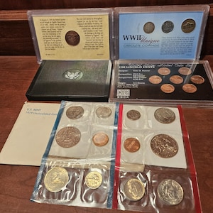 May include: A collection of US coins in various denominations and years, including a 1979 uncirculated coin set, a 1993 Lincoln Cent set, and a WWII Obsolete Coinage set. The coins are displayed in plastic sleeves and black cardboard cases.