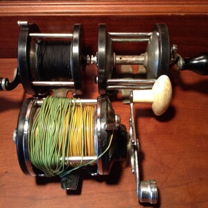 May include: Three vintage fishing reels with black, green, and yellow spools of line. The reels are made of metal and have a chrome finish.