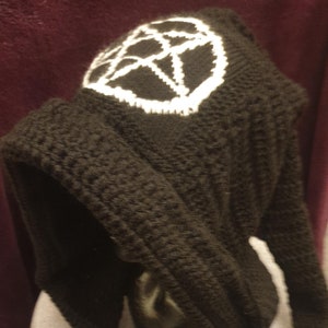 May include: Black knitted hooded hat with a white crocheted pentagram design. The hat has long black tassels.