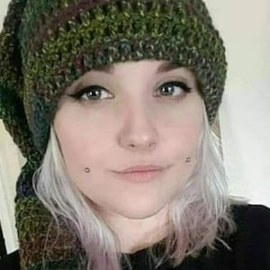 May include: A slouchy beanie hat crafted from variegated yarn in shades of forest green, olive, brown, and black. The knit texture features a ribbed pattern throughout the fabric, creating a thick and warm appearance for this headwear accessory.