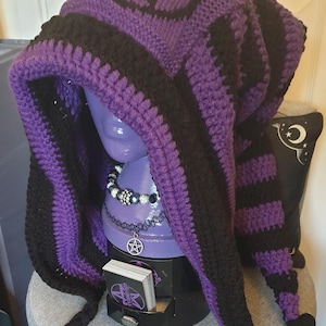 May include: Purple and black crocheted hooded hat with long tassels. The hat features a black pentagram design.