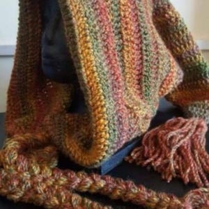 May include: A crocheted hooded scarf featuring a variegated yarn pattern in shades of orange, green, yellow, and brown. The accessory includes long, thick braided ties that extend from the hood, each finished with a large, textured yarn tassel.