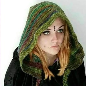 Pode incluir: Um capuz de crochê com um padrão de fio matizado em tons de verde, castanho e vermelho escuro. O capuz é feito com um ponto texturizado e usado sobre uma peça preta. O design inclui painéis laterais longos que caem sobre os ombros.