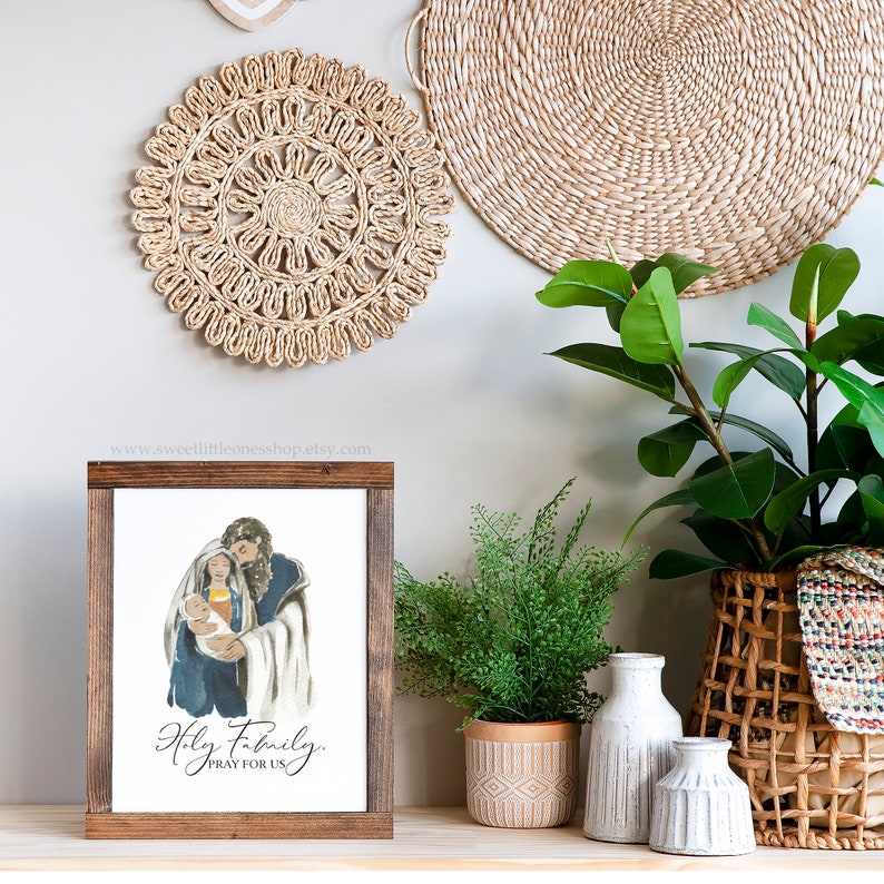 May include: A framed print with a watercolor illustration of the Holy Family. The image shows Mary, Joseph, and baby Jesus. The text below the image reads "Holy Family, Pray for Us".