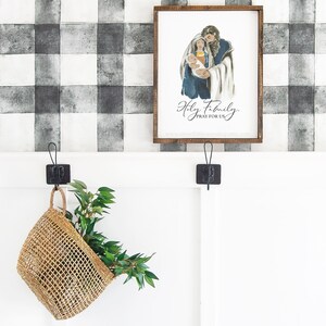 May include: A framed watercolor painting of the Holy Family with the text "Holy Family, Pray for Us" and a website address below. The painting is hanging on a black and white checkered wall.
