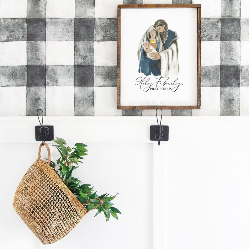 May include: A framed watercolor painting of the Holy Family with the text "Holy Family, Pray for Us" and a website address below. The painting is hanging on a black and white checkered wall.