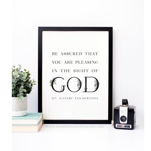 Op de afbeelding: Zwart-witte printbare quote art met bloemmotieven. De quote luidt "Wees ervan verzekerd dat je God behaagt. Heilige Kateri Tekakwitha."