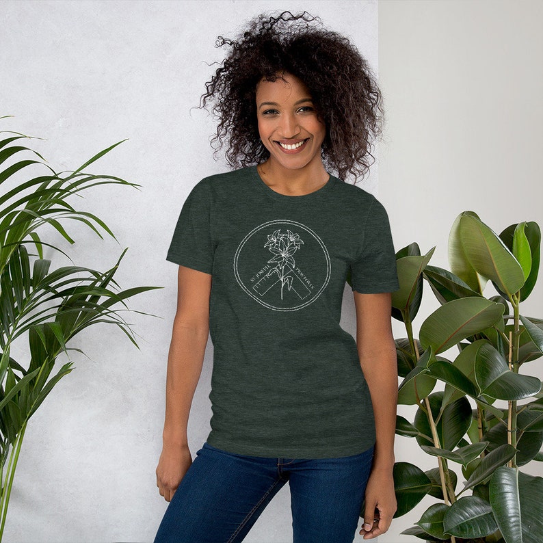 May include: Dark green t-shirt with a white circular graphic featuring a floral design and the text "St. Joseph Protect Us". The shirt is made of a soft material and has short sleeves.
