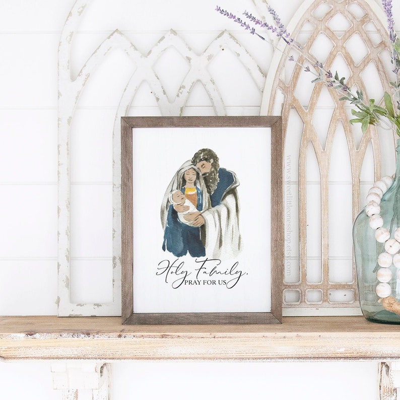 May include: A watercolor painting of the Holy Family, Mary, Joseph, and baby Jesus. The painting is framed in a brown wood frame and has the text "Holy Family, Pray for Us" written below the image.