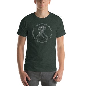 May include: Dark green t-shirt with a white circular graphic. The graphic features a lily flower design, a ruler, and the text "ST. JOSEPH PRAY FOR US" in a circular arrangement. The shirt is made of a soft material.