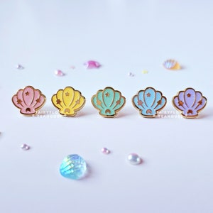 Puede incluir: Cinco pines de concha de mar de esmalte dorado con un diseño de estrella. Las conchas son en tonos de rosa, amarillo, verde y morado.