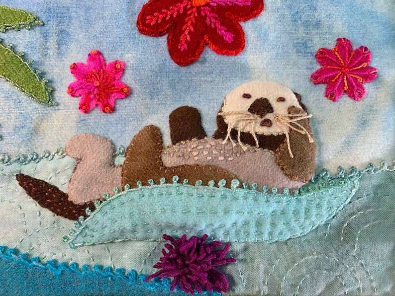 May include: A brown and gray sea otter with a white face and whiskers is floating on its back on a blue and green wave. The otter is surrounded by pink and red flowers.