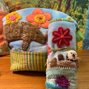 May include: Two blue fabric pouches with embroidered flowers and animals. The larger pouch has a brown rhinoceros and a yellow flower. The smaller pouch has a brown sea otter and a red flower.