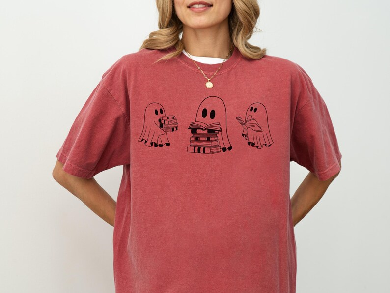 May include: A red t-shirt featuring a graphic of three ghosts holding books. The ghosts are black and white and the text on the shirt reads "Bookish Ghosts".