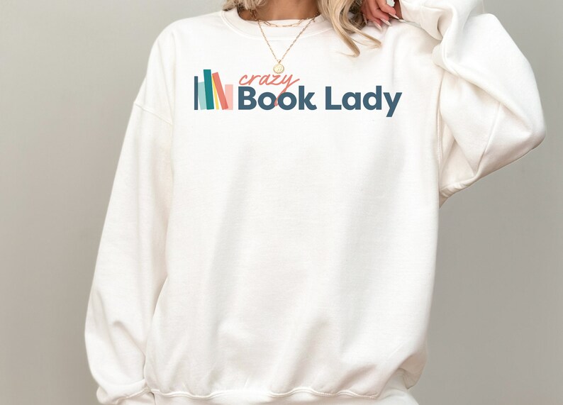 K&ouml;nnte beinhalten: Wei&szlig;er Pullover mit einer bunten Grafik von gestapelten B&uuml;chern und dem Text "crazy Book Lady".