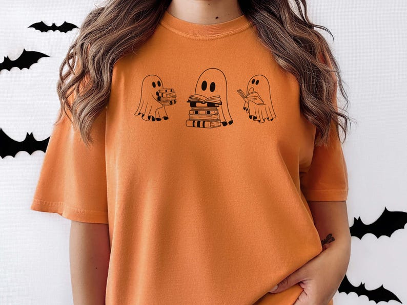 May include: Orange t-shirt featuring a graphic of three ghosts. The ghosts are holding books and one is reading a book. The text on the shirt says "Bookish Boo"