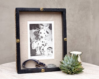 May include: Black wood picture frame with a black and white photo of a Dalmatian puppy. The frame has brass accents and a rope border. A blue leather dog collar and a brass tag are in front of the frame.