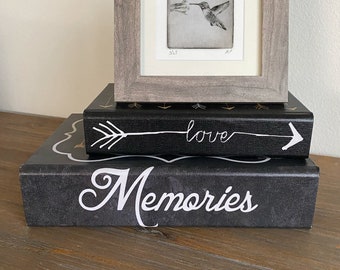 May include: A framed black and white print of a hummingbird in flight, sitting on top of two black books. The top book has the word "love" written on it with an arrow pointing to the right. The bottom book has the word "Memories" written on it.
