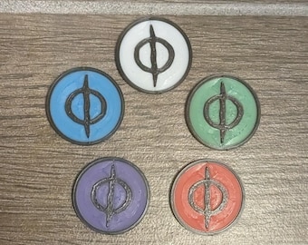 May include: Five round tokens with a black symbol on a wooden surface. The tokens are white, blue, green, purple, and orange.