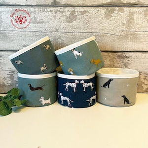 May include: A set of fabric storage baskets with dog-themed patterns. The baskets are in shades of blue, green, and beige, with white edging. The designs include Dachshunds, Dalmatians, Pugs, and other dog breeds.
