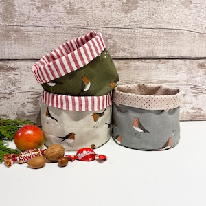 May include: Three fabric storage baskets in green, grey, and beige, each featuring a robin bird design. The rims are lined with red and white striped fabric. A red apple, walnuts, and sweets are in the foreground. Ideal for home storage.