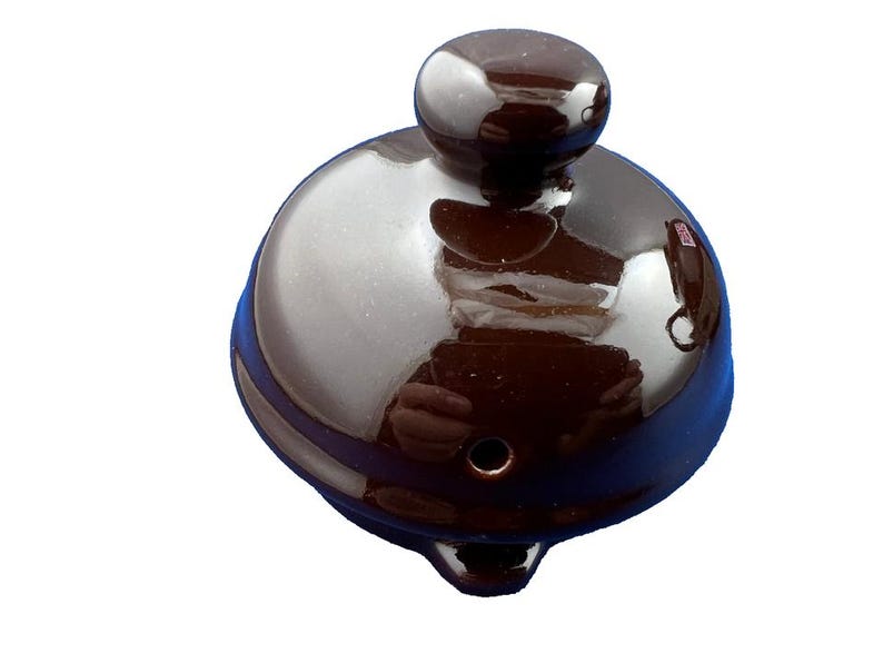 Puede incluir: Una tapa de tetera de cer&aacute;mica marr&oacute;n oscuro con un acabado brillante. La tapa tiene una parte superior redondeada con un peque&ntilde;o pomo y un pico curvo. La tapa est&aacute; dise&ntilde;ada para una tetera.