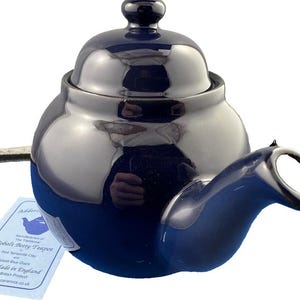 May include: A cobalt blue teapot with a matching lid and handle. The teapot has a glossy finish and a rounded shape. A tag attached to the teapot reads "Cobalt Betty Teapot" and "Hand Made in England".