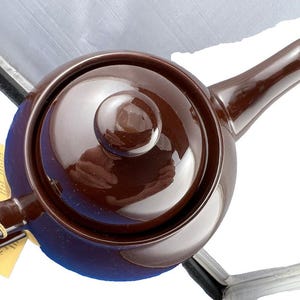 Puede incluir: Una tetera de cer&aacute;mica marr&oacute;n con tapa y boquilla a juego. La tetera tiene un cuerpo redondeado y un asa lateral. Una etiqueta amarilla est&aacute; sujeta al asa. Para preparar t&eacute;.