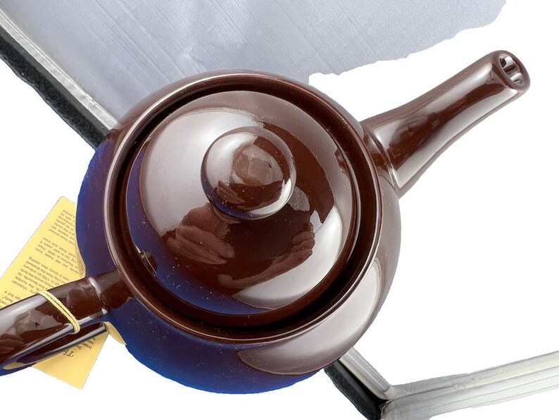 Puede incluir: Una tetera de cer&aacute;mica marr&oacute;n con tapa y boquilla a juego. La tetera tiene un cuerpo redondeado y un asa lateral. Una etiqueta amarilla est&aacute; sujeta al asa. Para preparar t&eacute;.