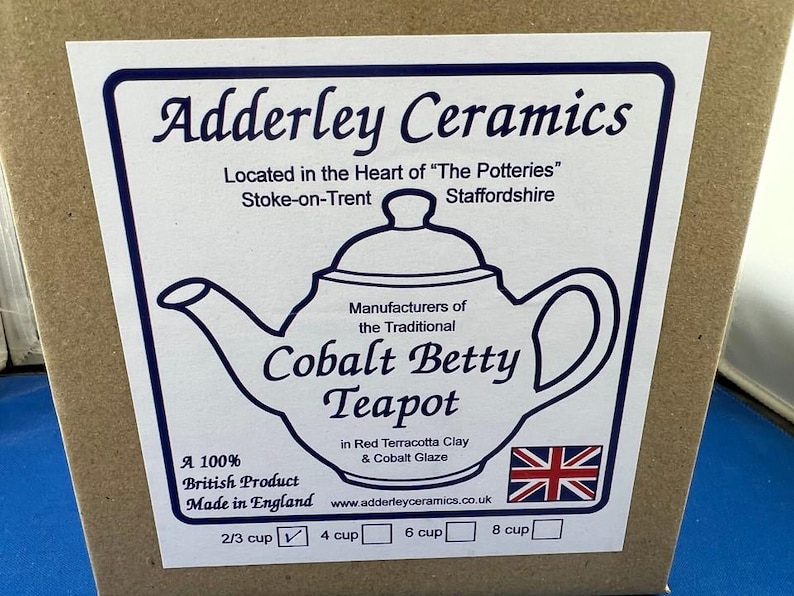 May include: A label on a cardboard box features the text "Adderley Ceramics" and a drawing of a teapot. The label states the teapot is the "Cobalt Betty Teapot" made in England. The label also includes the British flag.
