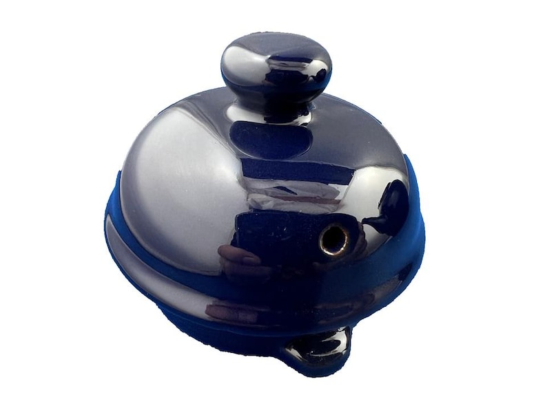 May include: A shiny, navy blue teapot lid with a silver-colored, reflective surface. The lid has a small, rounded handle on top and a blue band around the base. The design is simple and elegant.