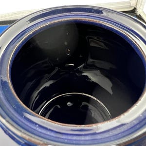 May include: A close-up view of a dark blue ceramic teapot. The interior is a deep, glossy blue, contrasting with the lighter blue rim. The teapot is set against a blue and white background.