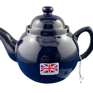 May include: A navy blue ceramic teapot with a matching lid and handle. The teapot has a glossy finish and a small sticker with the Union Jack flag and the words "Made in England". A tag is attached to the handle.