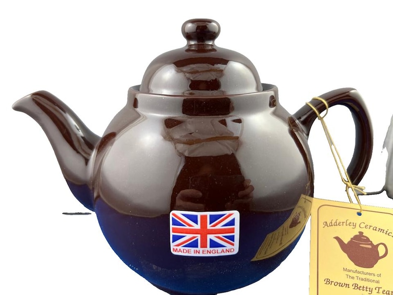Puede incluir: Una tetera de cer&aacute;mica marr&oacute;n con cuerpo redondeado, boquilla y asa. La tetera tiene una tapa con un peque&ntilde;o pomo y una pegatina con la bandera de la Union Jack que dice "Made in England". Una etiqueta dice "Adderley Ceramic" y "Brown Betty Teapot".
