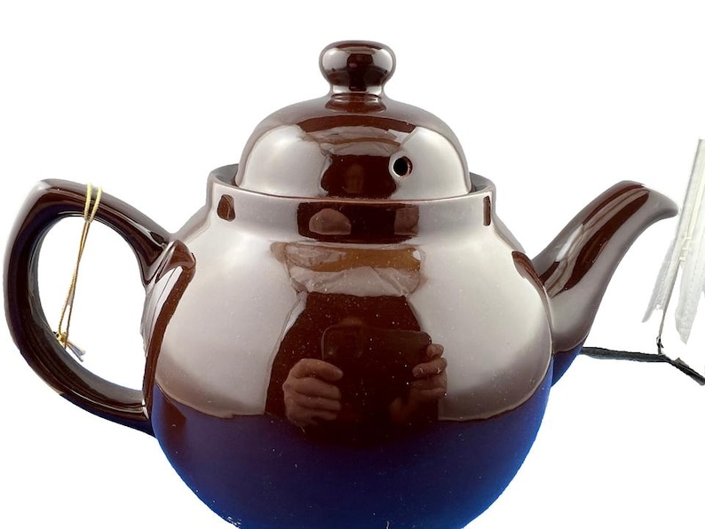 Puede incluir: Una tetera de cer&aacute;mica marr&oacute;n con tapa y asa a juego. La tetera tiene un acabado brillante y una base azul oscuro. Una cuerda dorada est&aacute; sujeta al asa. La tetera est&aacute; dise&ntilde;ada para preparar t&eacute;.