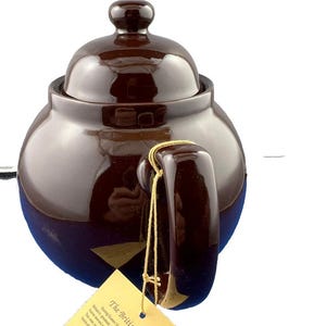 Puede incluir: Tetera de cer&aacute;mica marr&oacute;n con tapa y asa. La tetera tiene un acabado brillante y una forma redondeada. Una etiqueta est&aacute; sujeta al asa con un cord&oacute;n dorado. La tetera est&aacute; dise&ntilde;ada para preparar t&eacute;.
