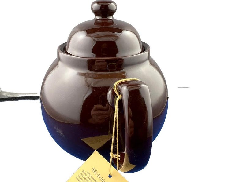 Puede incluir: Tetera de cer&aacute;mica marr&oacute;n con tapa y asa. La tetera tiene un acabado brillante y una forma redondeada. Una etiqueta est&aacute; sujeta al asa con un cord&oacute;n dorado. La tetera est&aacute; dise&ntilde;ada para preparar t&eacute;.