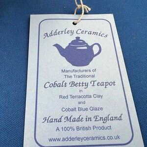May include: A light blue tag with the text "Adderley Ceramics" and "Cobalt Betty Teapot" in a stylized font. The tag also states "Hand Made in England" and "A 100% British Product". A teapot illustration is also visible.