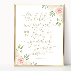 Puede incluir: Una impresión enmarcada con letras doradas que dice "Por este niño he orado y el Señor ha concedido el deseo de mi corazón" con el versículo bíblico 1 Samuel 1:27. La impresión está decorada con flores de acuarela en rosa y blanco.