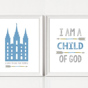 May include: Two white framed prints with blue and silver text and arrows. The left print features a blue silhouette of a temple with the text "I love to see the temple". The right print features the text "I am a child of God".