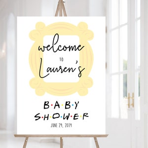 May include: A white welcome sign with a yellow frame, similar to the iconic frame from the TV show "Friends". The sign says "Welcome to Lauren's Baby Shower" with the date June 29, 2019.