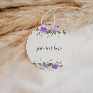 May include: A round, white gift tag with a purple floral design and the text "your text here".