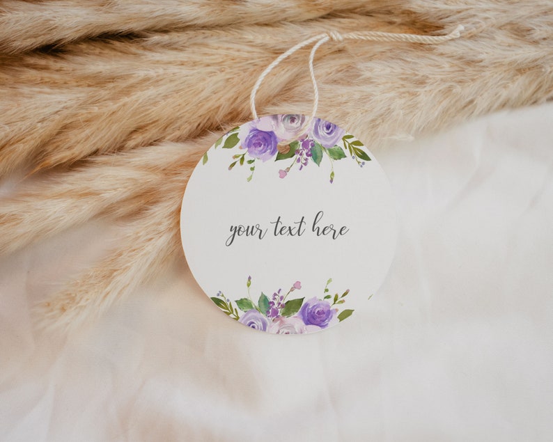 May include: A round, white gift tag with a purple floral design and the text "your text here".
