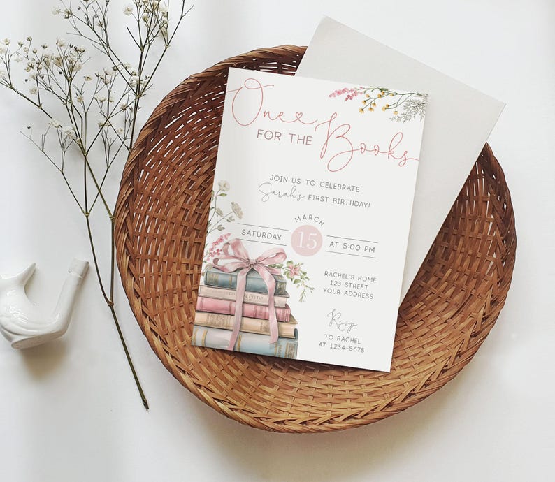 K&ouml;nnte beinhalten: Eine wei&szlig;e Einladung mit rosa und gr&uuml;nen floralen Akzenten. Der Text lautet "One for the Books" und enth&auml;lt Details f&uuml;r eine erste Geburtstagsfeier. Die Einladung zeigt einen Stapel B&uuml;cher, die mit einem rosa Band zusammengebunden sind.