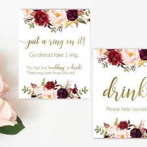 K&ouml;nnte beinhalten: Zwei bedruckbare Schilder mit einem Blumendesign in den Farben Burgunderrot, Rosa und Gr&uuml;n. Das obere Schild sagt "put a ring on it! Go ahead take 1 ring... "Do Not Say 'wedding' or 'bride'." "Steal rings from those who do!" Das untere Schild sagt "drinks Please help yourself"