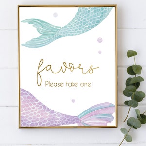 May include: A printable sign with a gold glitter font that says "favors" and "Please take one". The sign is decorated with two watercolor mermaid tails, one teal and one purple.